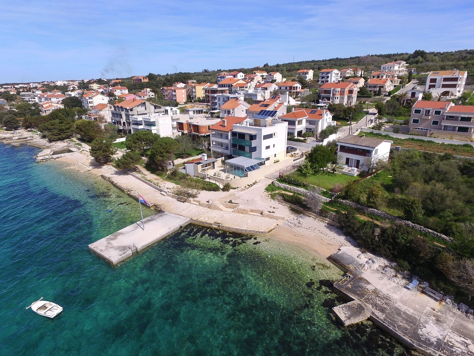 A coastal residential area with houses, clear blue water, and a boat docked near the shore.