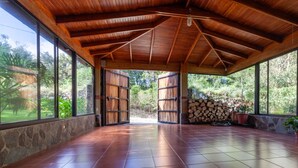 A spacious covered patio with a wooden ceiling, large windows, and a stone wall. - Monteverde Panoramic House (Monteverde)