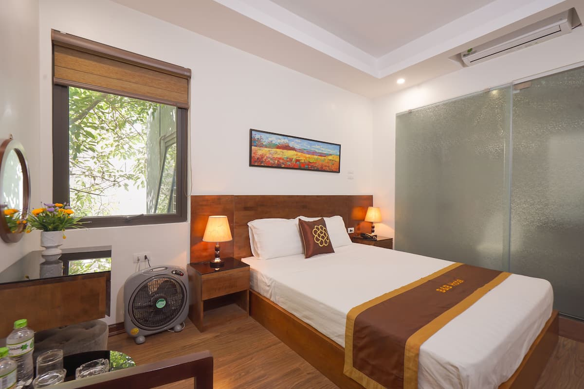 Une chambre d’hôtel avec un lit, des lampes de chevet, un ventilateur, une fenêtre donnant sur un paysage agréable et un tableau au mur.