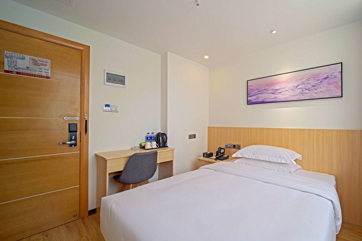 Habitación de hotel con cama, escritorio, silla, mesita de noche y un cuadro en la pared.