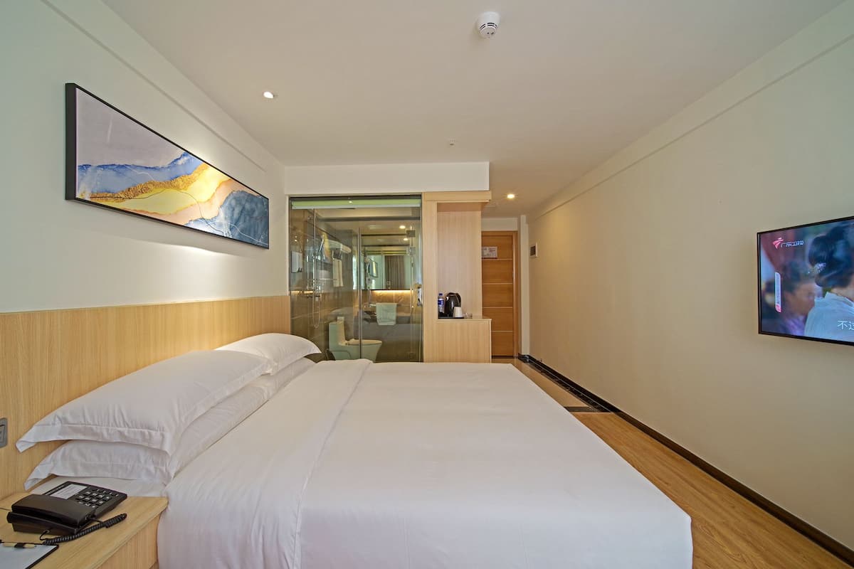 Habitación de hotel con una cama grande, teléfono en la mesita de noche, televisor y baño visible a través de una puerta de cristal.