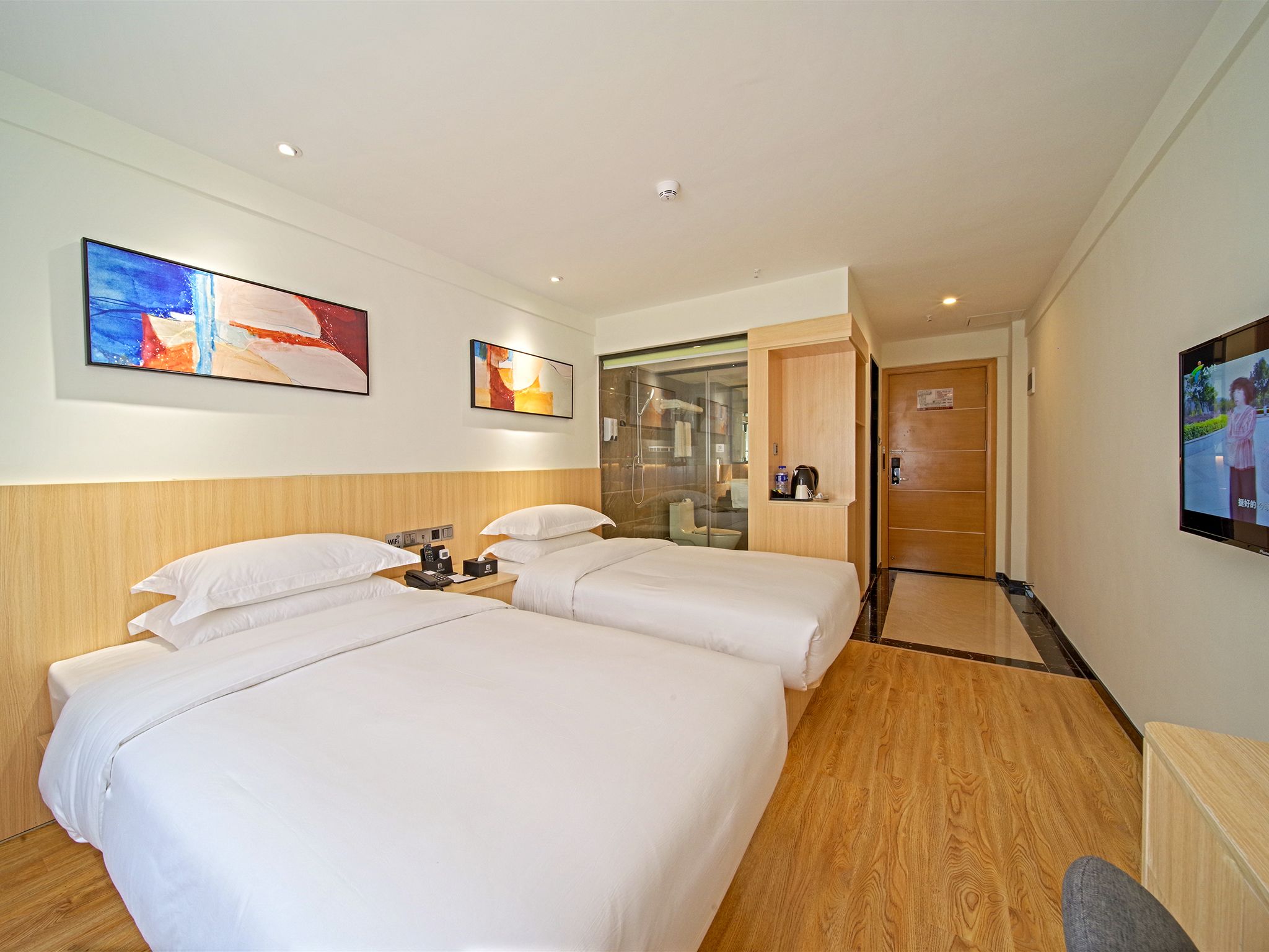 A hotel room with two beds, a shower area, and artwork on the walls.