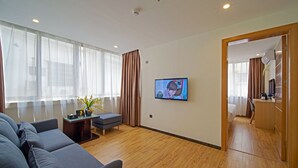 A modern hotel room with a large sofa, a small table with a vase of flowers, a television mounted on the wall, and a wooden floor. - Guangzhou Changxing Xintiandi Hotel (Guangzhou)