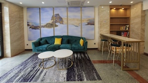 A modern living room with a teal sofa, two white round tables, a large abstract painting, and a wooden bookshelf. - Guangzhou Changxing Xintiandi Hotel (Guangzhou)