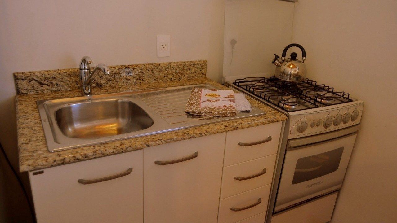 A compact kitchen with a granite countertop, stainless steel sink, and a gas stove.