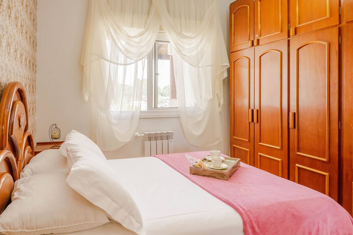 A bedroom with a wooden bed, white bedding, a pink blanket, and a tray with a cup and saucer.