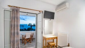Un dormitorio con cama, una mesita de noche de madera, un espejo y vistas a un balcón con mesa y sillas.