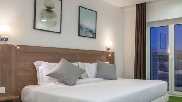 Une chambre d’hôtel avec un grand lit, deux lampes fixées au mur et une fenêtre avec des rideaux.