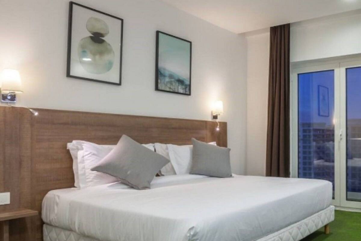 Een hotelkamer met een groot bed, twee wandlampen en een raam met gordijnen.