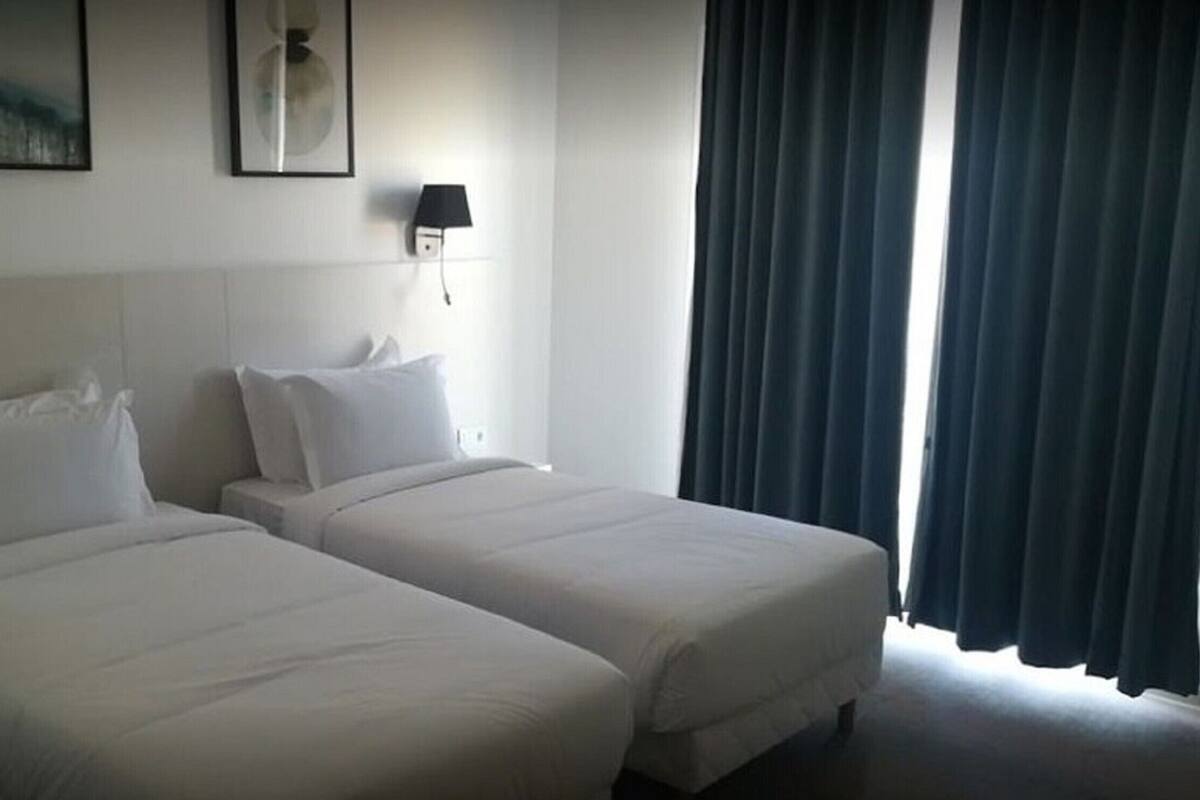 Een hotelkamer met twee éénpersoonsbedden, een nachtkastje, een lamp en een raam met gordijnen.