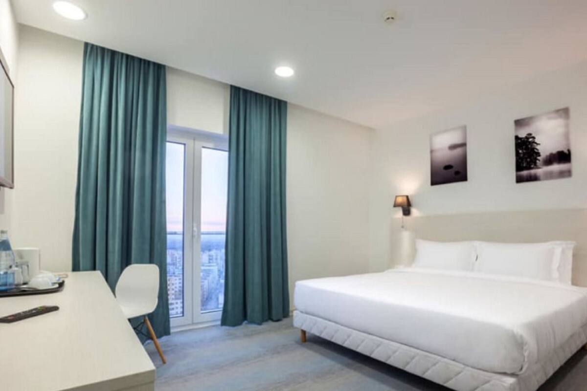 Hotelkamer met een bed, bureau, stoel, raam met gordijnen en wandlampen.