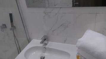 Un baño con un lavamanos blanco, un espejo encima y una toalla a la derecha.