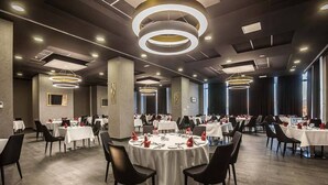 Une salle de banquet spacieuse, avec des tables rondes dressées pour le repas, un éclairage moderne et une palette de couleurs neutres.