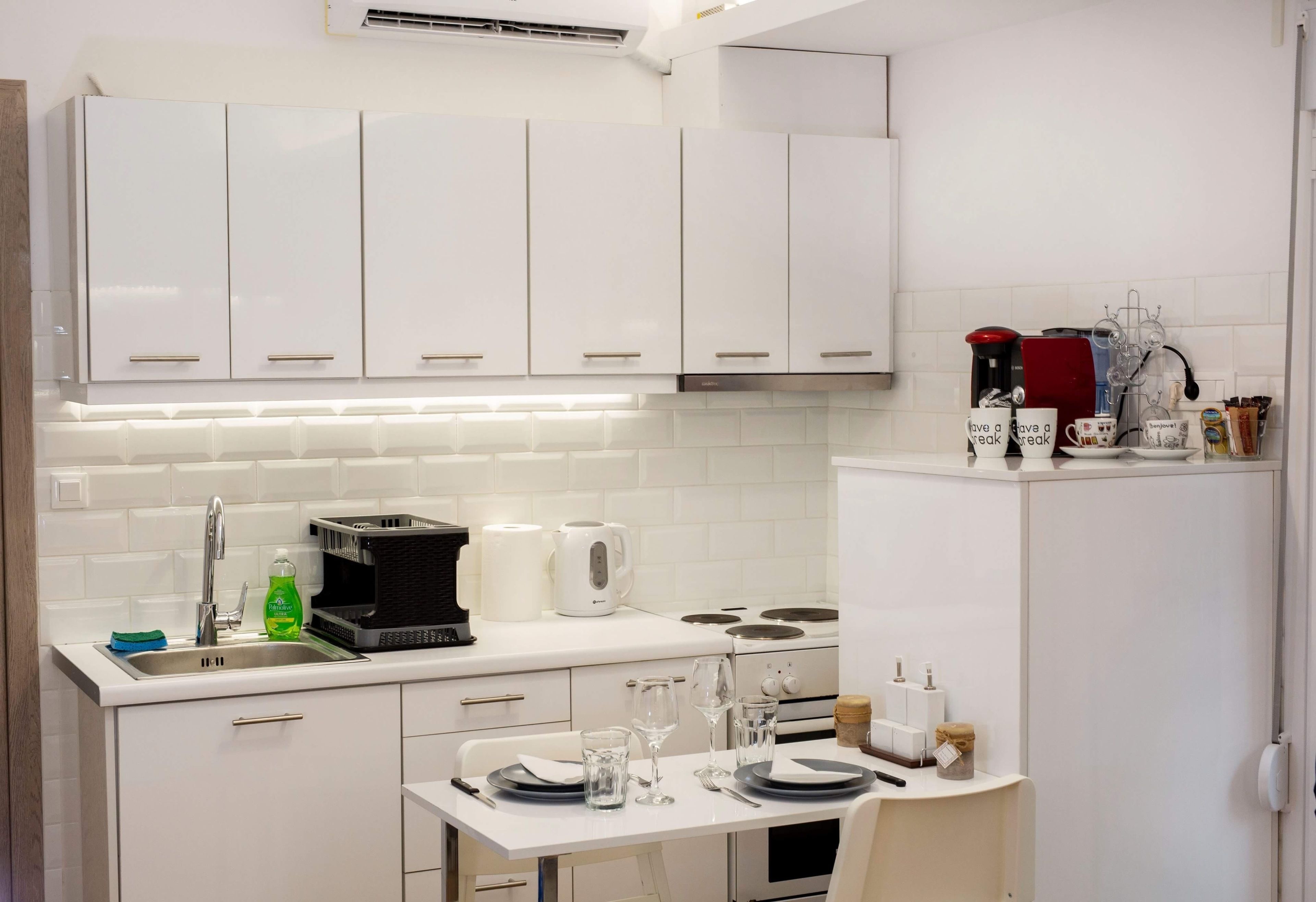 Une cuisine moderne avec des meubles blancs, un évier en acier inoxydable et un coin repas avec une table mise pour deux personnes.