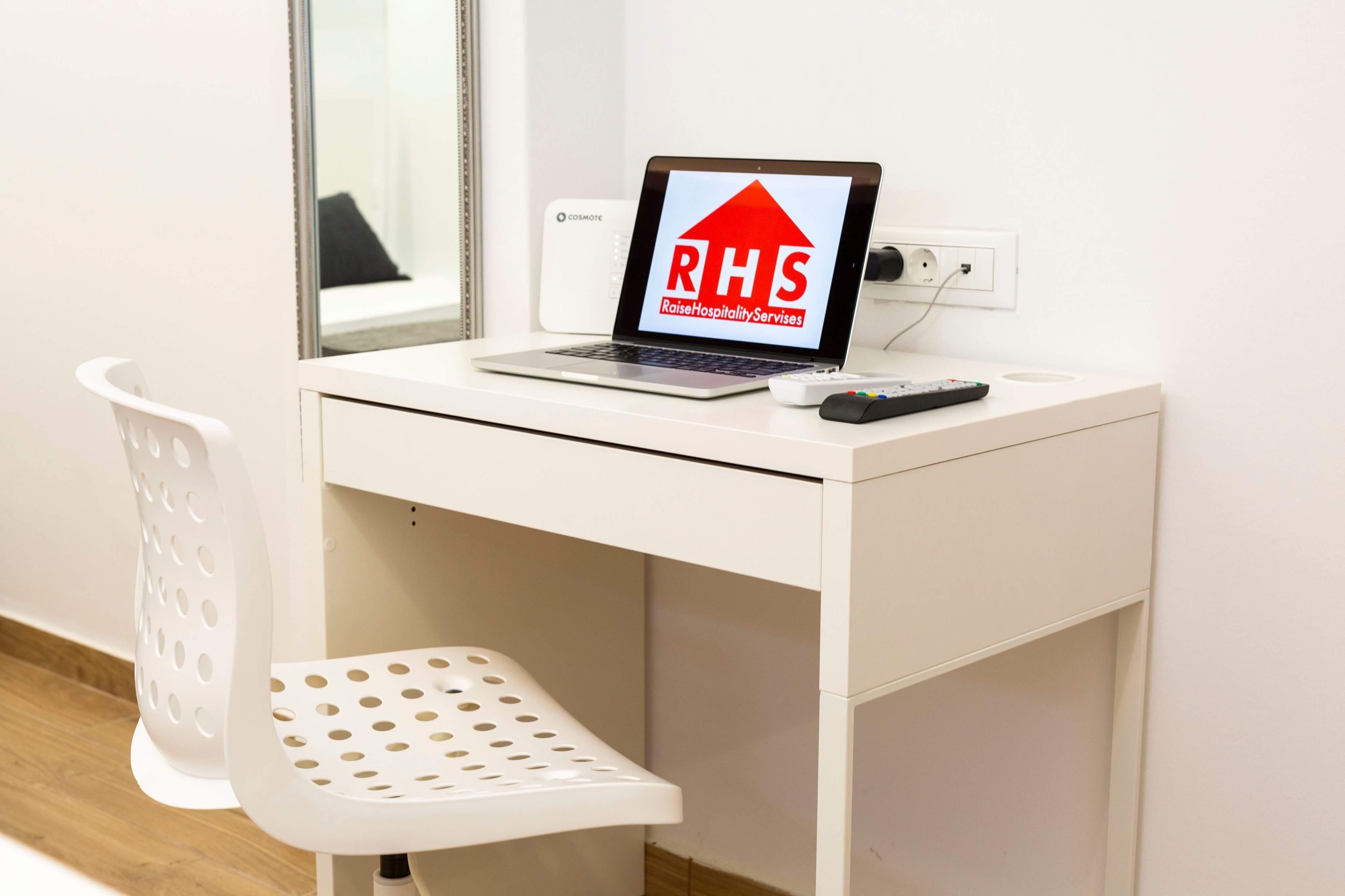A white desk with a laptop displaying "RHS Raise Hospitality Services" logo, a remote control, and a white chair with perforated design.