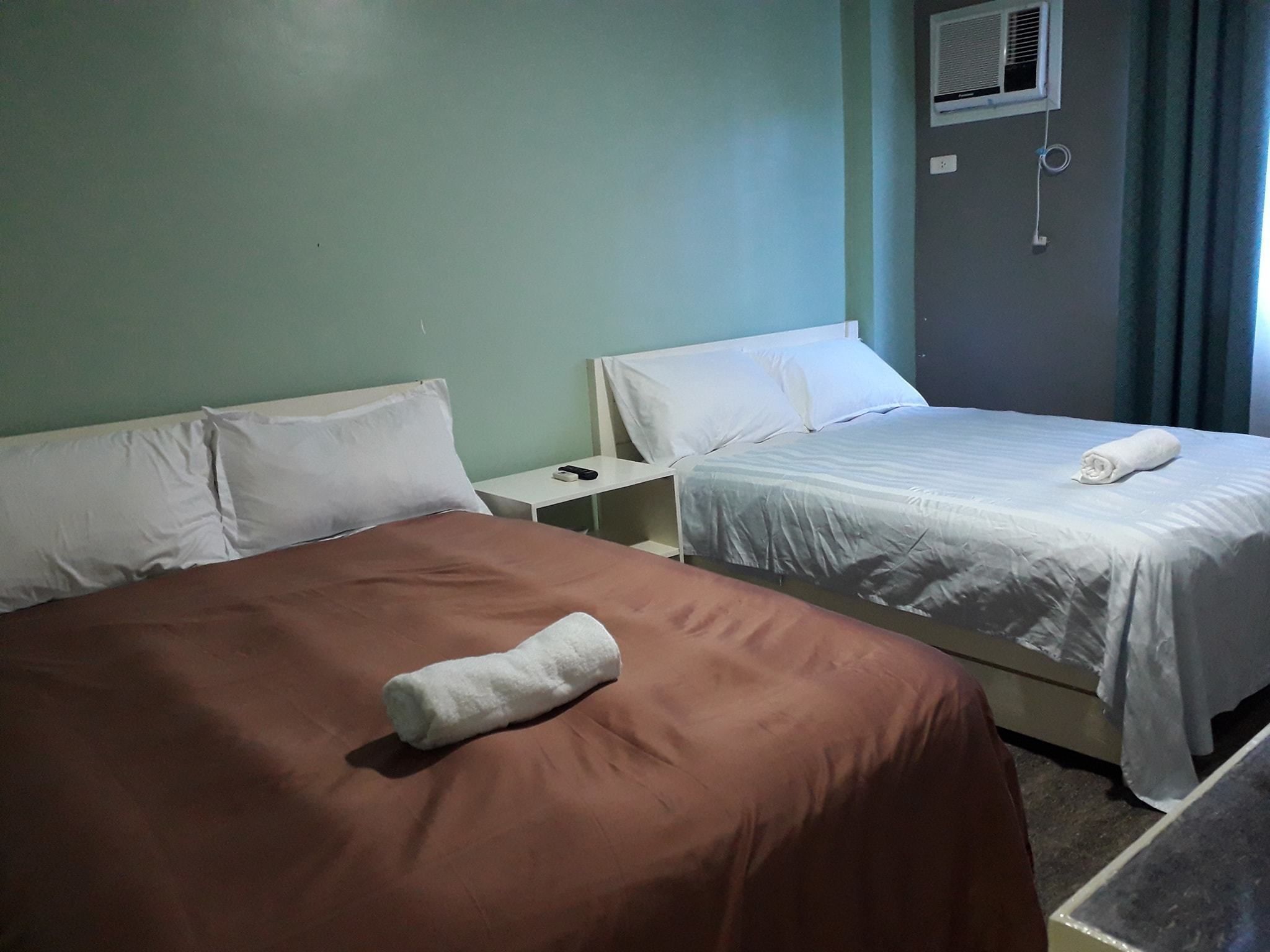 Habitación de hotel con dos camas, una mesita de noche pequeña y un equipo de aire acondicionado en la pared.