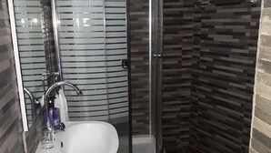 A bathroom with a glass shower enclosure, a white sink, and a tiled floor.