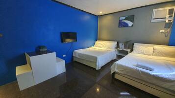 Habitación de hotel con dos camas, un televisor de pantalla plana montado en la pared, una mesita blanca y una pared decorada en azul.