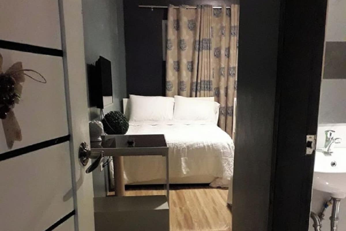 Ein Schlafzimmer mit einem Bett, einem Nachttisch, einer kleinen Pflanze und einem Vorhang.
