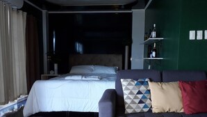 A modern bedroom with a large bed, a grey sofa, and a green accent wall.