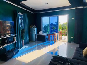 A modern living room with a flat-screen TV, a sofa, a coffee table, and a balcony with a view of greenery. - PhueNics De Galera (Puerto Galera)