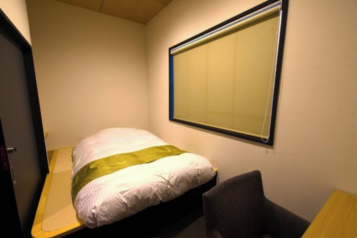 A small, single-bed room with a window, a desk, and a chair.