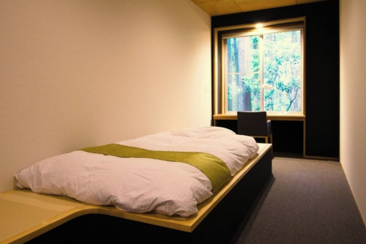 A single bed with a green accent, a window with a view of trees, and a chair.