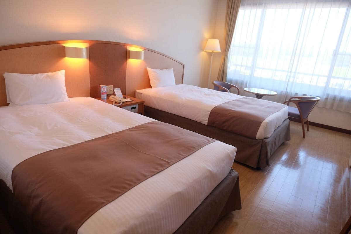 Ein Hotelzimmer mit zwei Betten, Nachttischlampen, einem kleinen Tisch und einem Sessel.