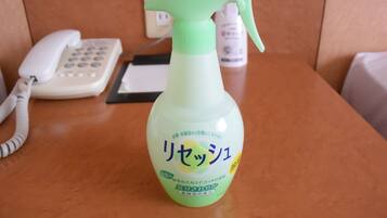 A spray bottle with Japanese text on a wooden surface, a white telephone, and a black object in the background.