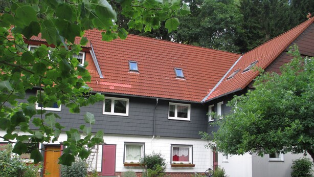 Ett tvåvåningshus med ett rött tegeltak, en röd dörr och en liten trädgård framför huset med gångar av grus.