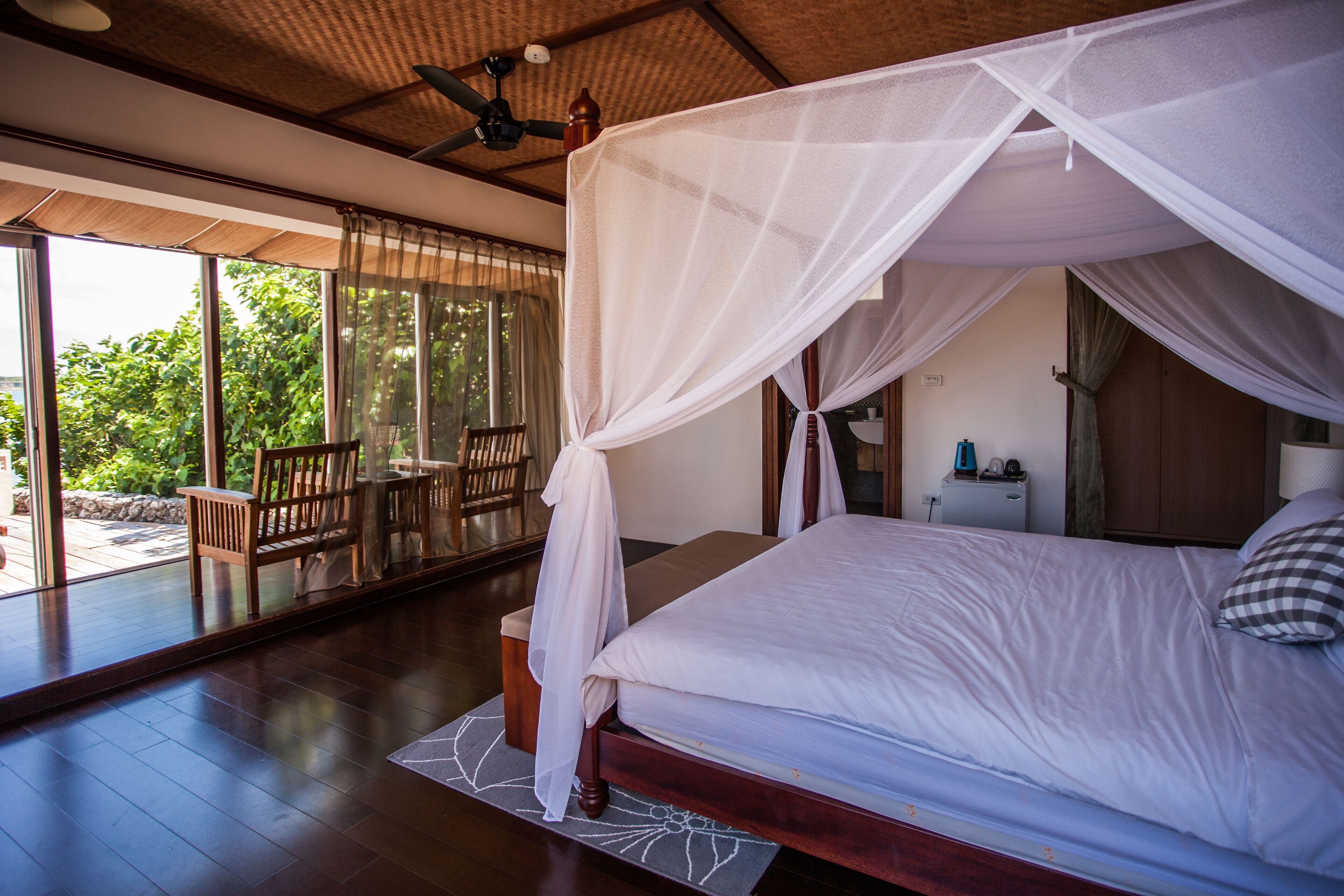 A bedroom with a canopy bed, wooden furniture, and a view of greenery outside.