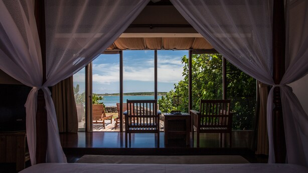 A bedroom with a large window overlooking a balcony with wooden furniture and a view of the sea. - Summer Ya B&B (Huxi)
