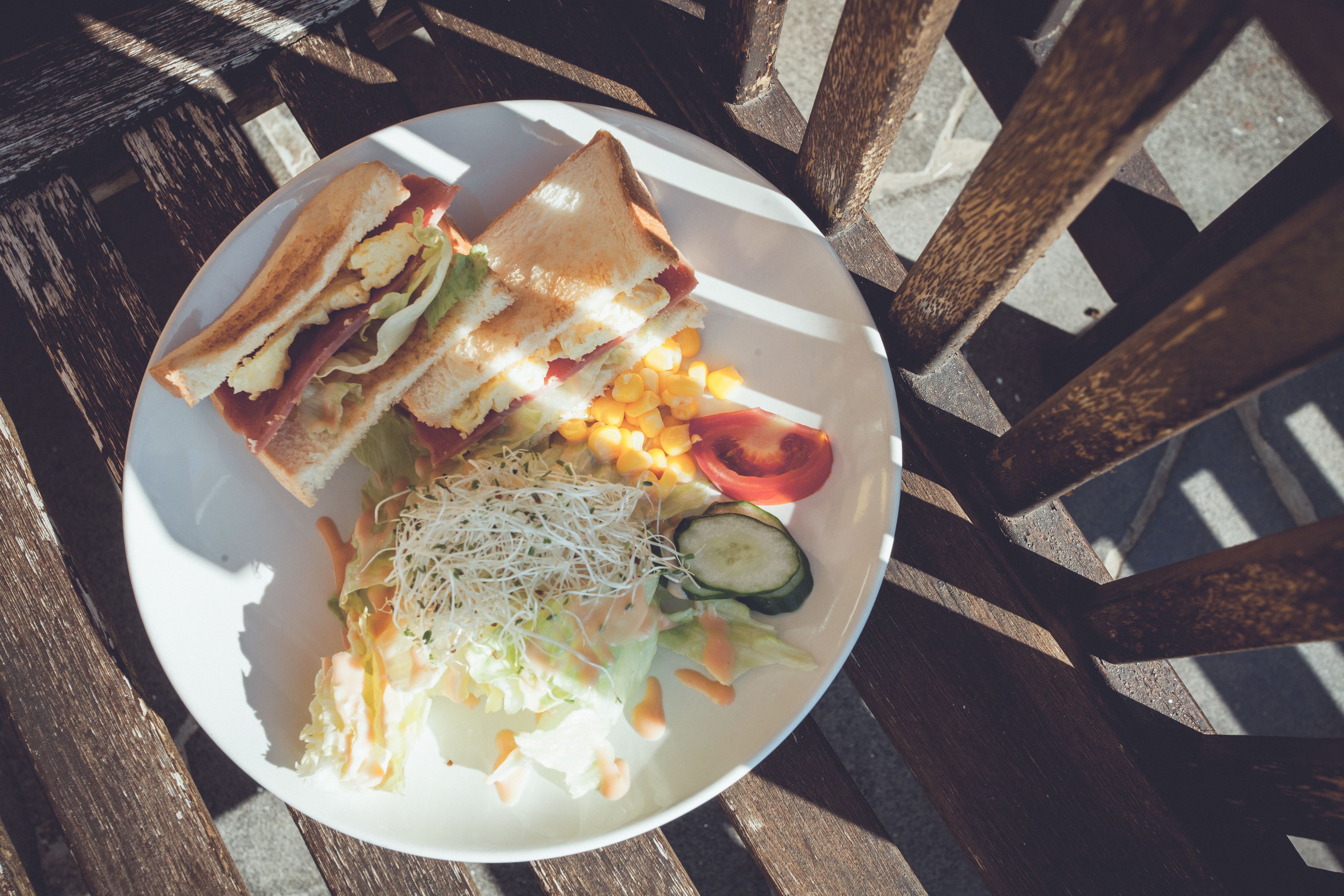Une assiette contenant un sandwich, une salade et des épis de maïs, posée sur une table en bois.