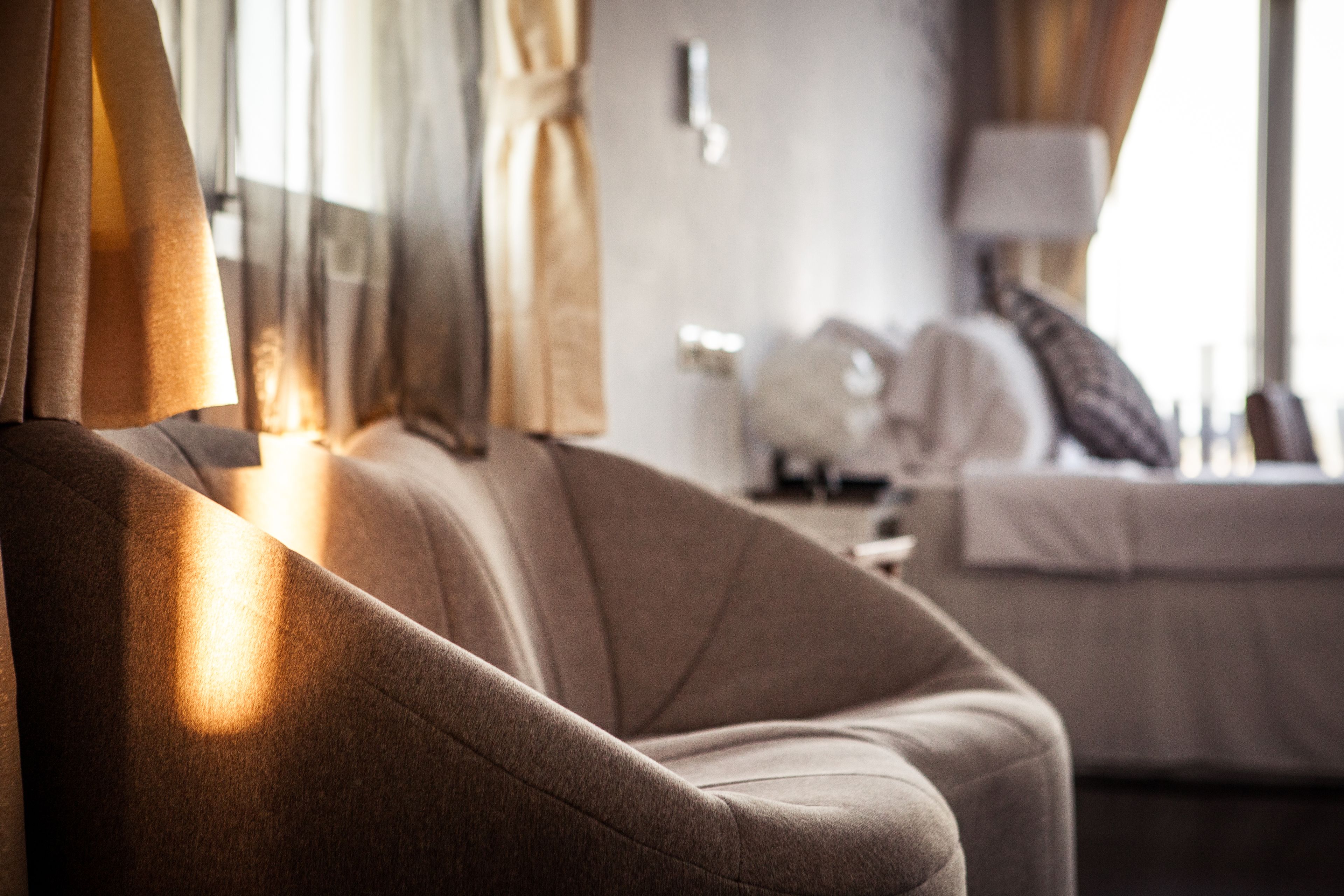 A close-up of a plush, beige sofa with a soft texture, positioned in a well-lit room with a bed in the background.