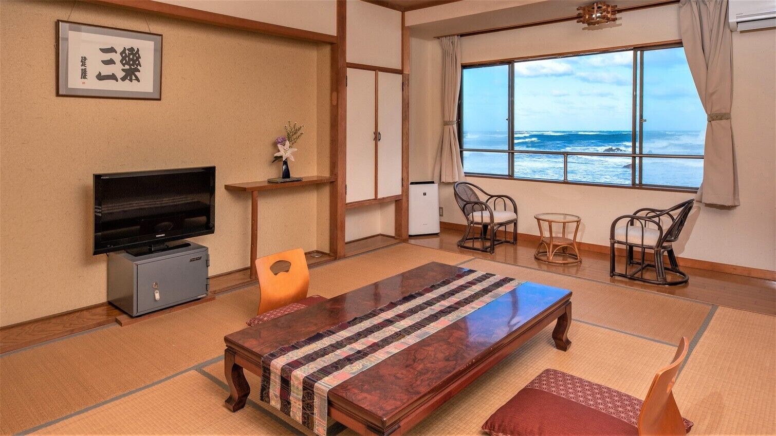 Habitació amb televisió, taula de fusta, cadires, vista a l'oceà i un sòl de tatami.
