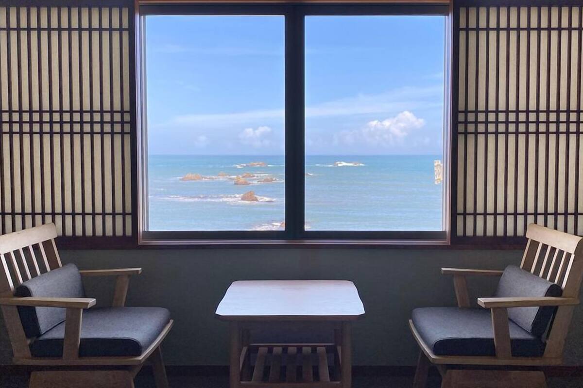 Une pièce avec une grande fenêtre, deux chaises et une petite table.