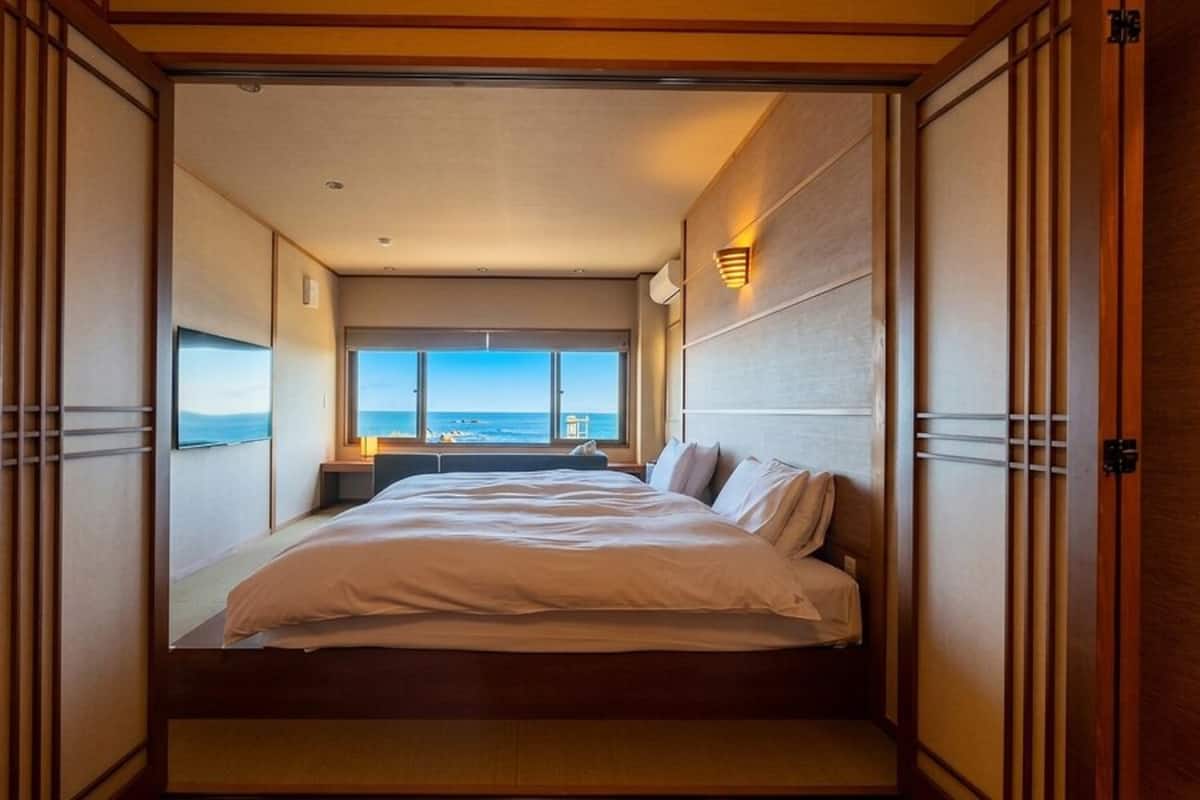 A room with a bed, a view of the sea, and sliding doors.