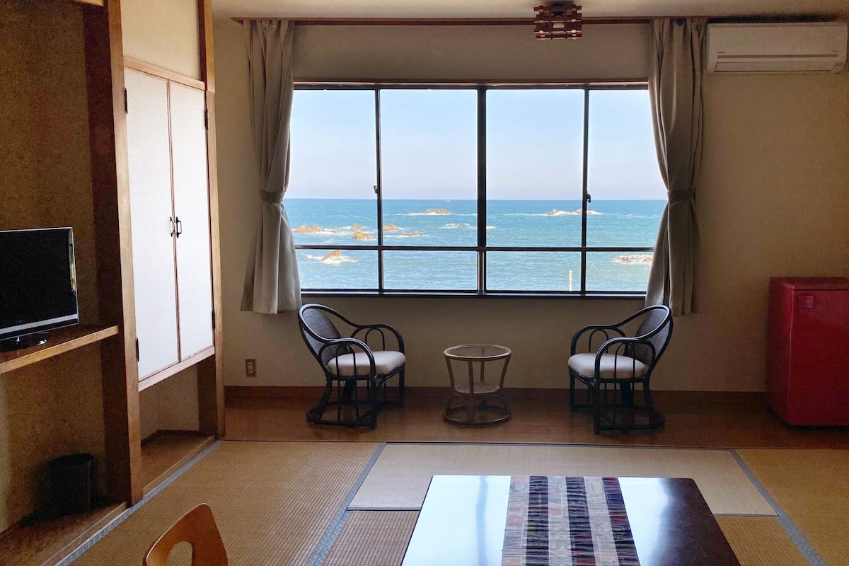 A room with a view of the sea, two chairs, a small table, a TV, and a red cabinet.