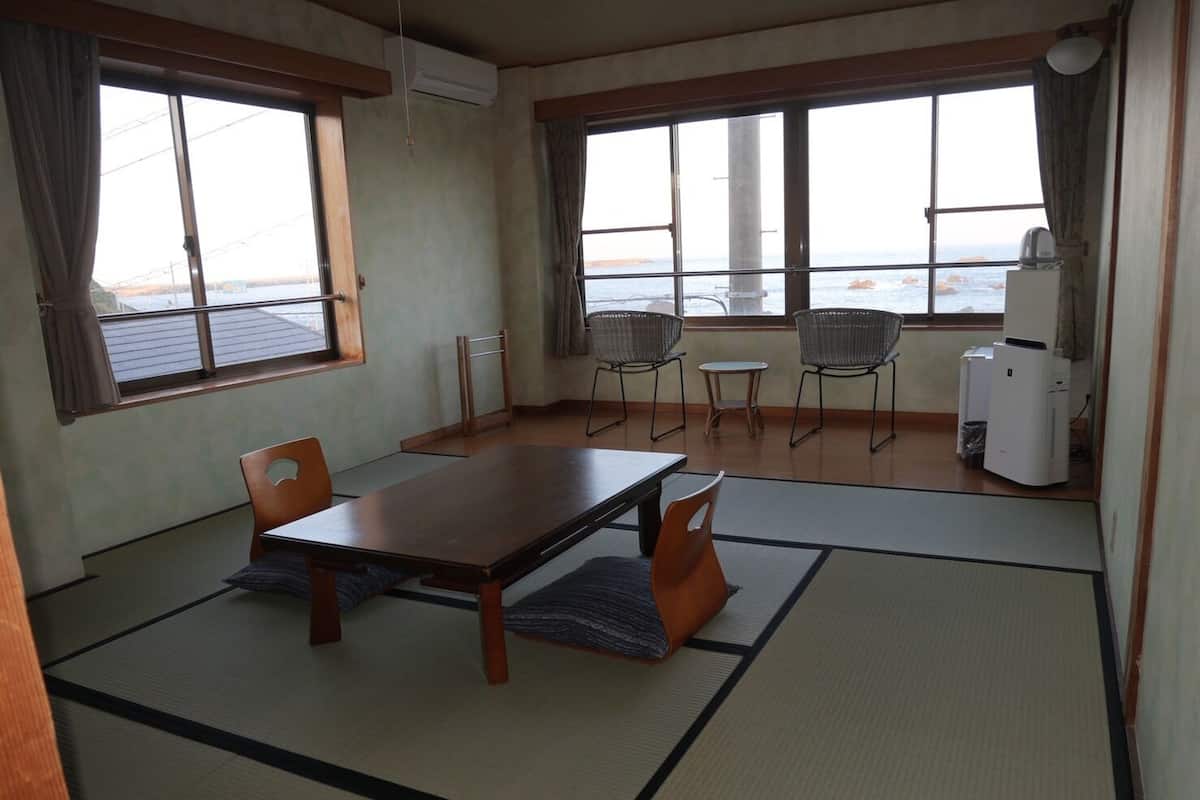 A room with tatami mats, a wooden table, two chairs, a small table, and a refrigerator.