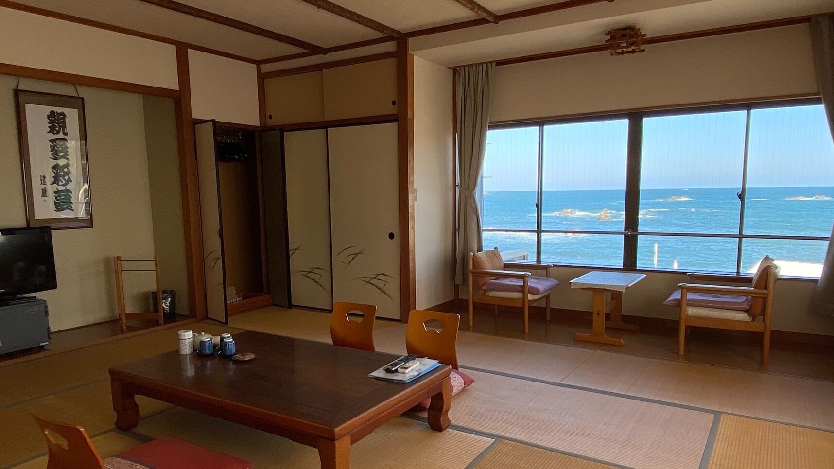 Habitació japonesa tradicional amb sòl de tatami, una taula baixa i cadires. Un gran finestral ofereix una vista a l'oceà.