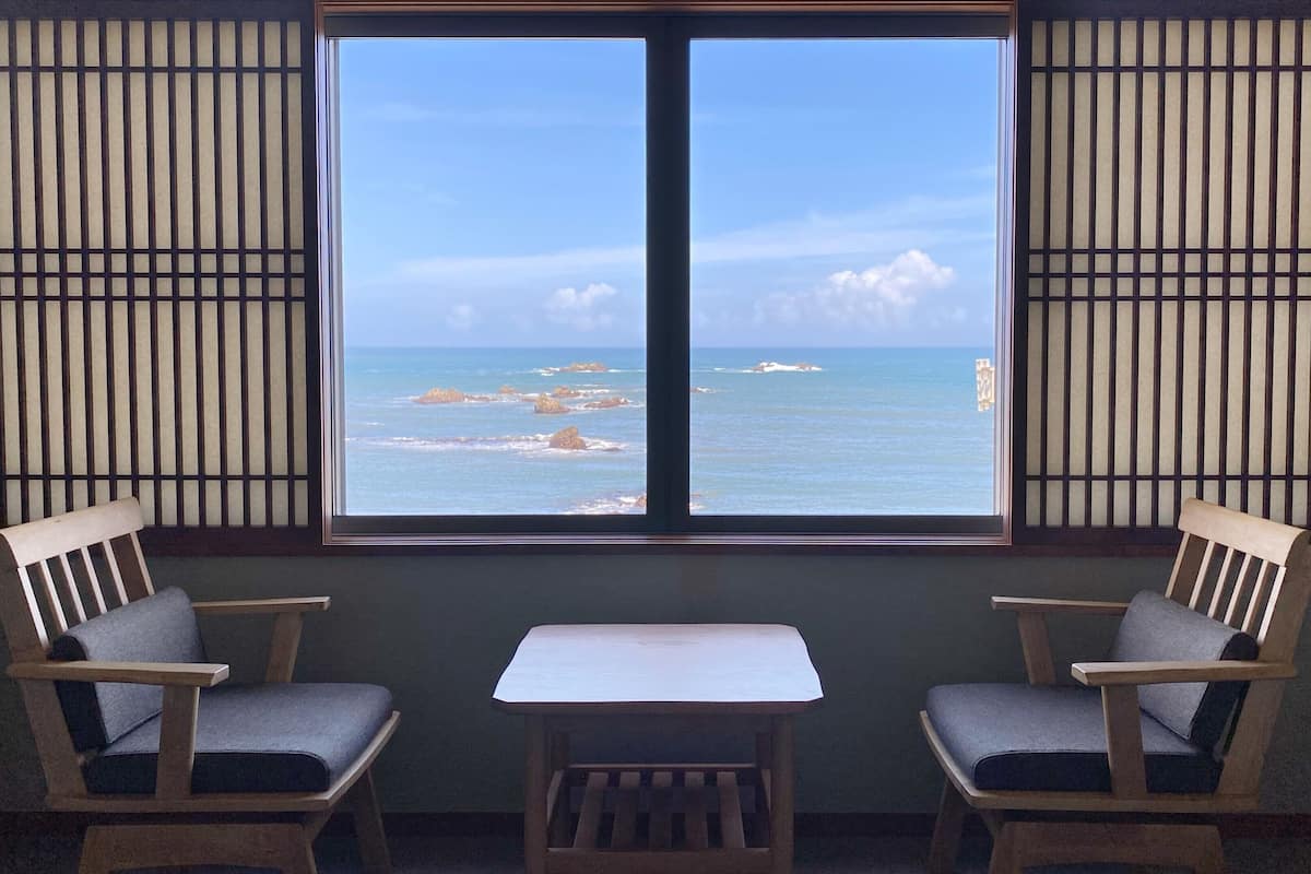 A room with a view of the ocean, two wooden chairs, and a small table.