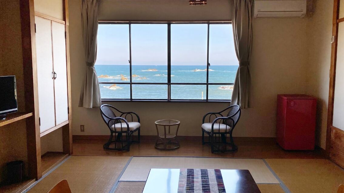 Habitació amb vista al mar, dues cadires, una taula petita, un televisor i un armari vermell.