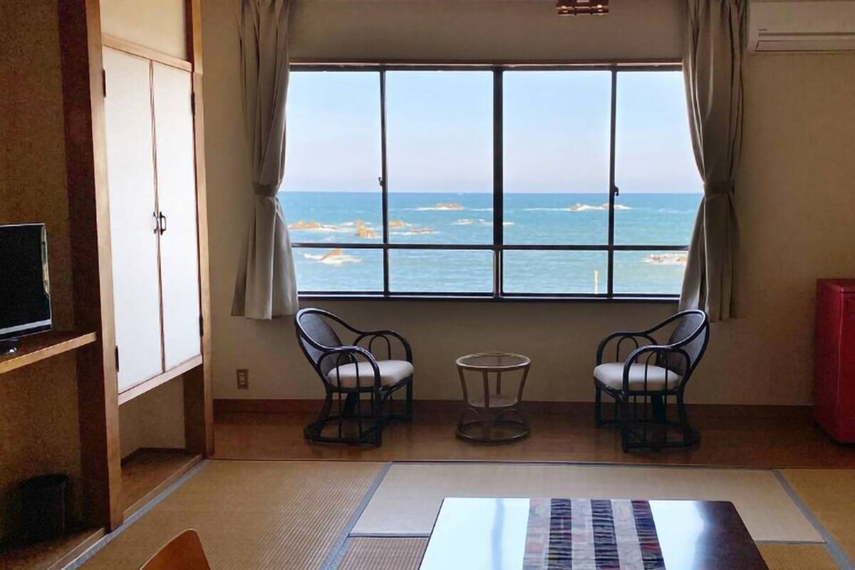 A room with a view of the sea, two chairs, a small table, a TV, and a red cabinet.