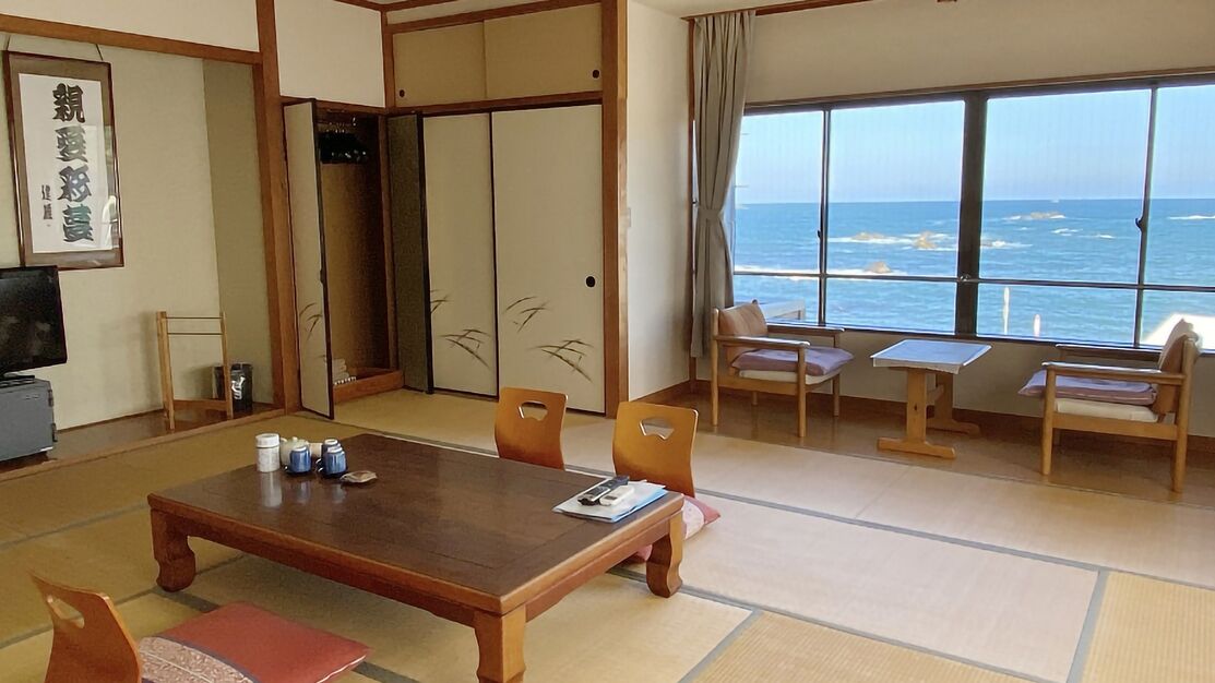 Habitació japonesa tradicional amb sòl de tatami, una taula baixa, cadires, una porta corredissa i vista al mar.