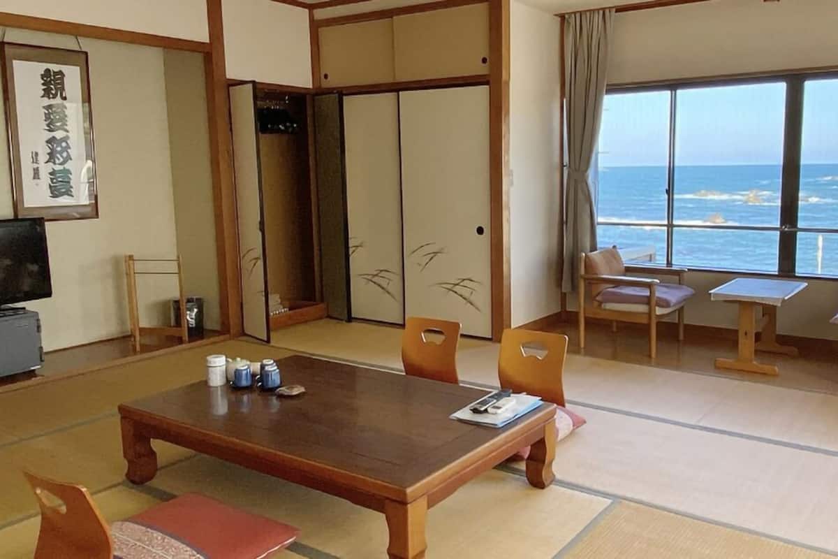 A traditional Japanese room with tatami flooring, a low table, chairs, a sliding door, and a view of the sea.