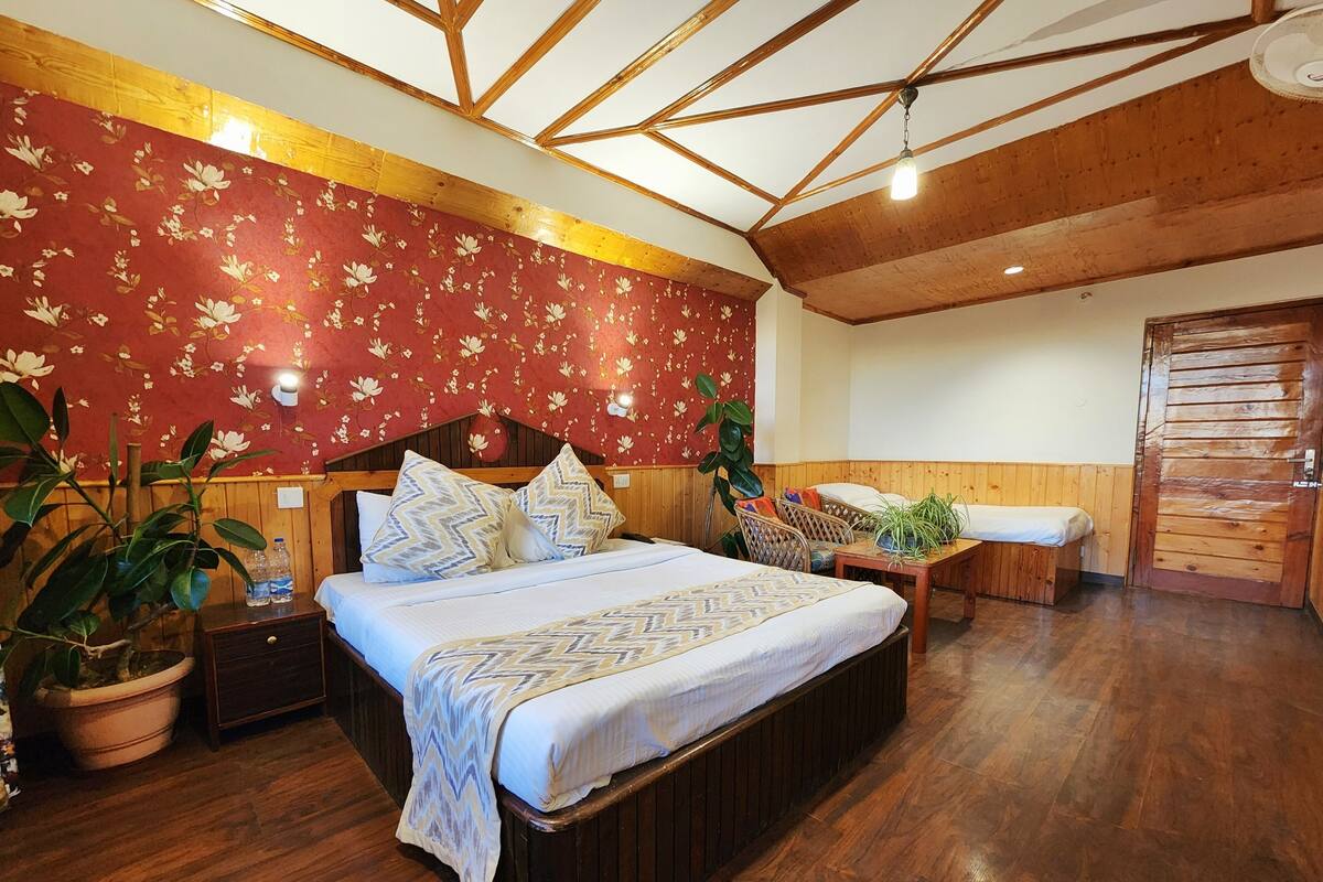 Quarto com teto de madeira, cama com roupa de cama estampada, um banco de madeira e um vaso com planta.