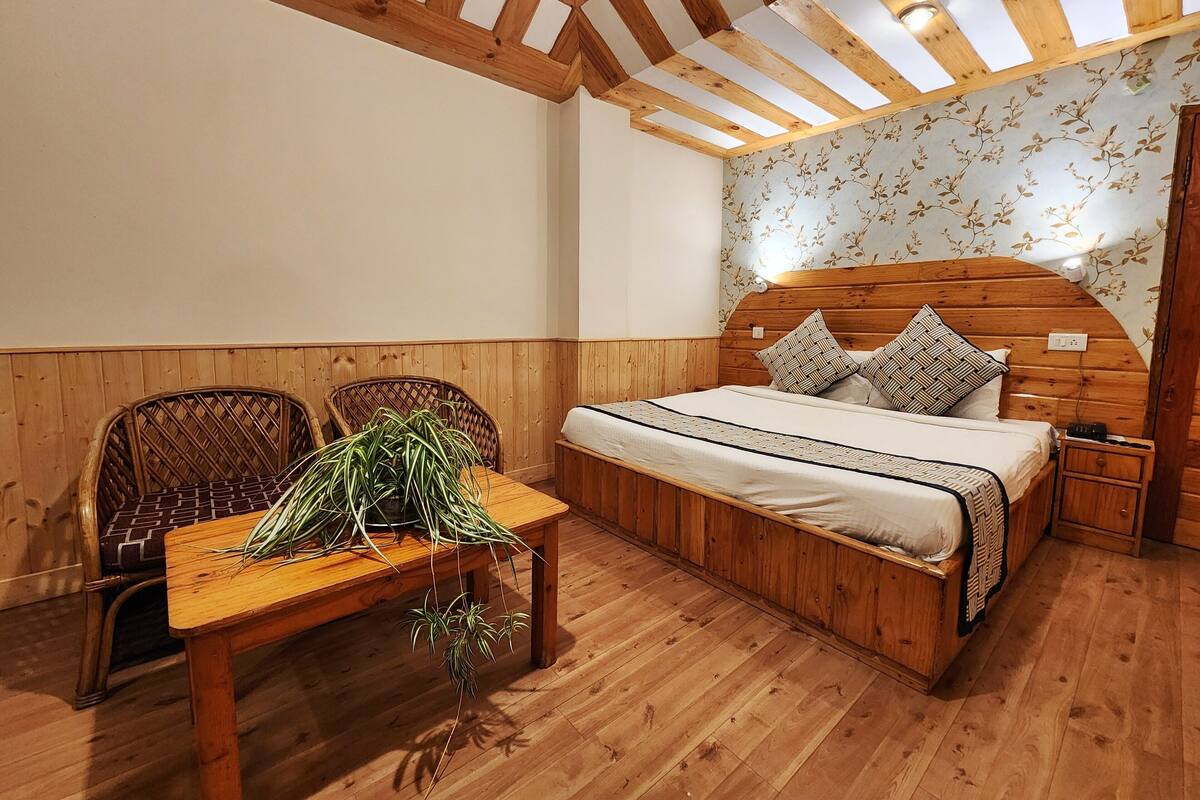 Um quarto com painéis de madeira, uma cama, uma mesa com plantas e duas cadeiras de vime.