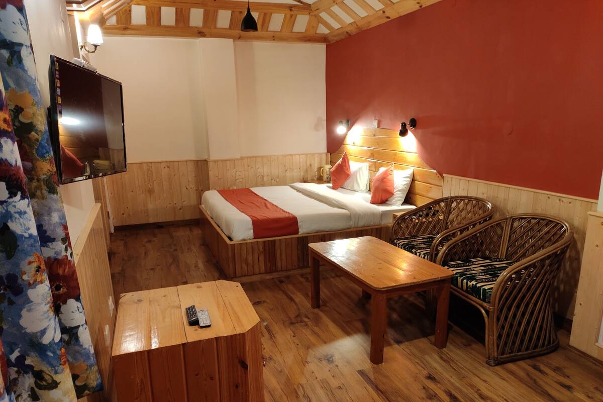 Quarto de madeira com uma cama, uma mesa, uma cadeira e uma televisão presa à parede.