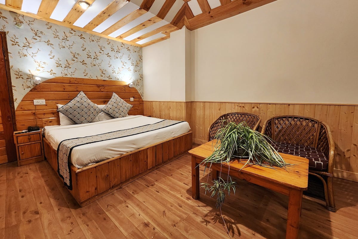 Quarto com estrutura de madeira, cama, mesas de cabeceira, uma mesa com plantas e cadeiras de vime.