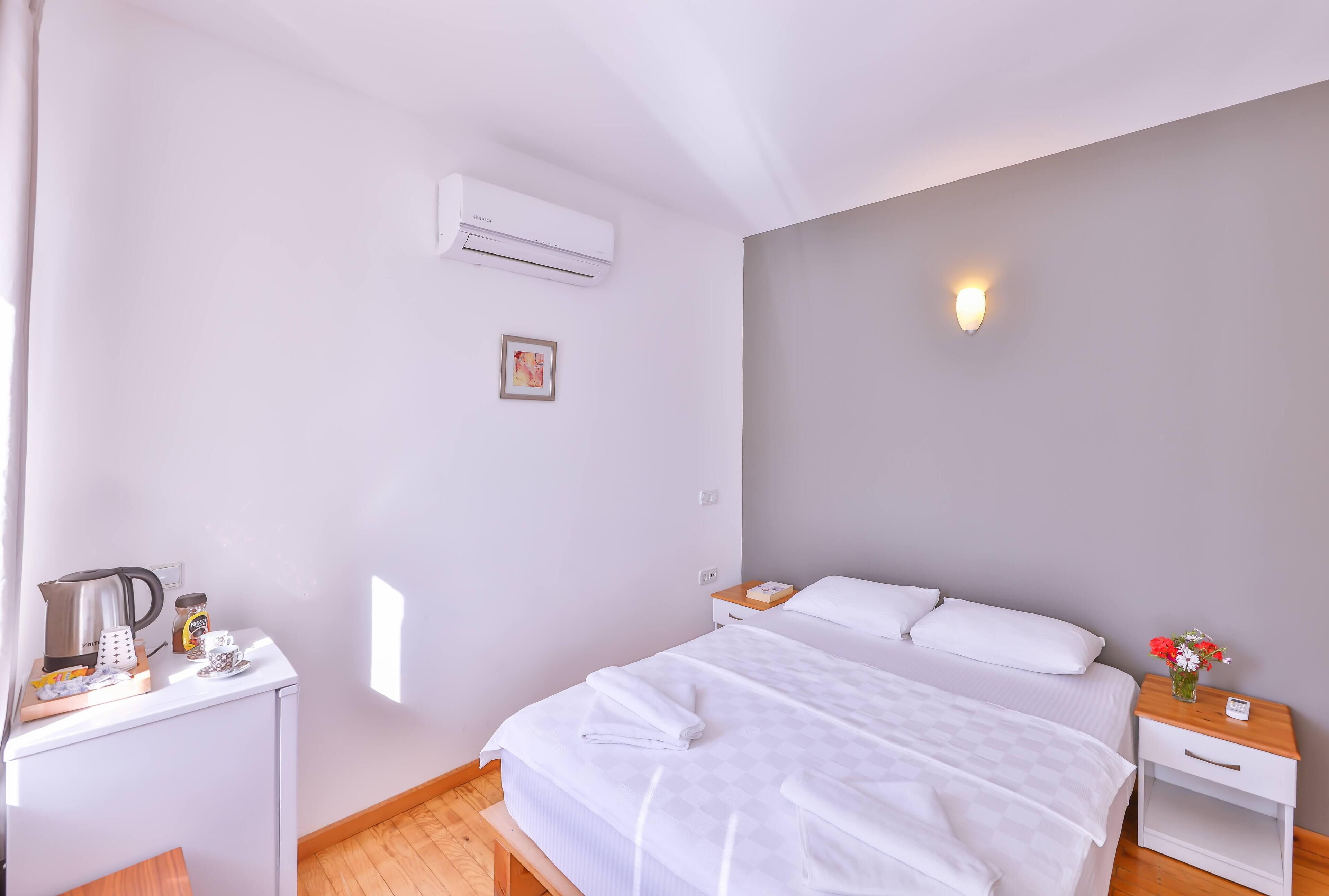 Habitación de hotel con cama, mesita de noche y un pequeño escritorio con tetera, taza de café y tarro.
